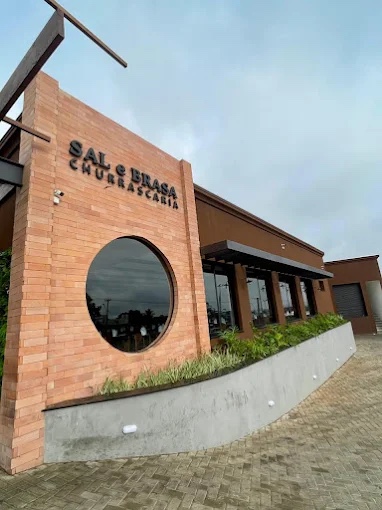 Fachada em tijolo aparente com janela circular e letreiro Sal e Brasa